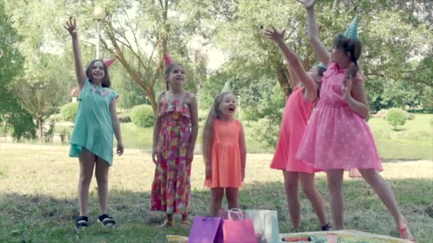 Flickor firar sin födelsedag i parken och slänger godis. Varm solig dag. — Stockvideo