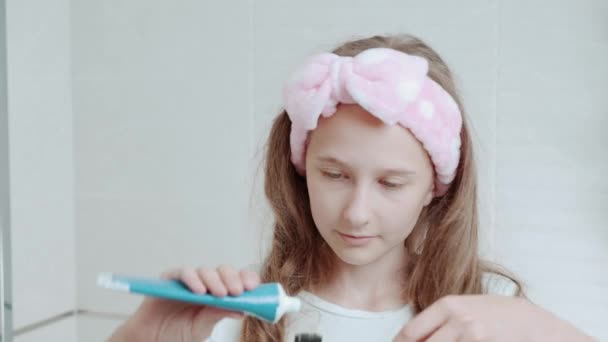 En söt flicka applicerar tandkräm på en ekologisk svart borste, borstar tänderna. — Stockvideo