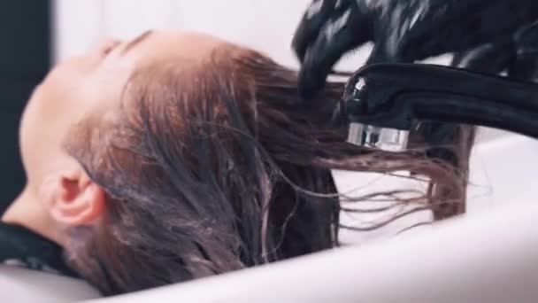 Ο κομμωτής πλένει το κεφάλι μιας νεαρής όμορφης πελάτισσας με νερό.. — Αρχείο Βίντεο