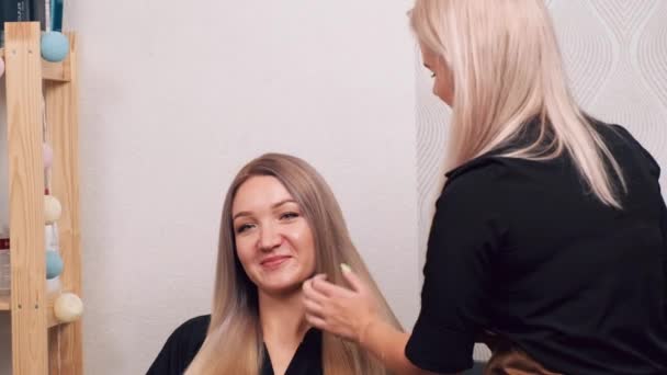 Vrouwelijke kapper kamt lang blond haar uit. Het meisje kwam naar de schoonheidssalon.. — Stockvideo