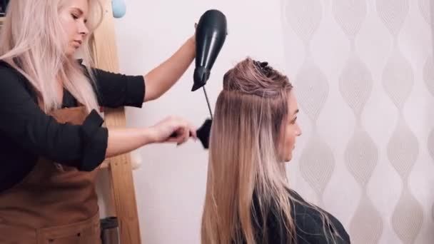 Jovem mulher secar o cabelo com um secador de cabelo em um salão de beleza, fazer o cabelo. — Vídeo de Stock