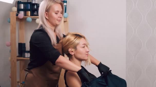 Junge Frau legt Friseur peignoir auf die Kundin auf die Kundin. — Stockvideo