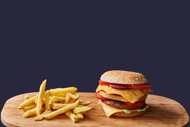 Hafif ahşap bir masada patates kızartmasının yanında büyük sulu bir hamburger. Koyu arkaplan.