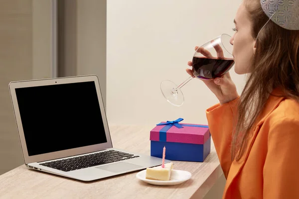 Una donna comunica online il giorno del suo compleanno con un bicchiere di vino in mano. — Foto Stock