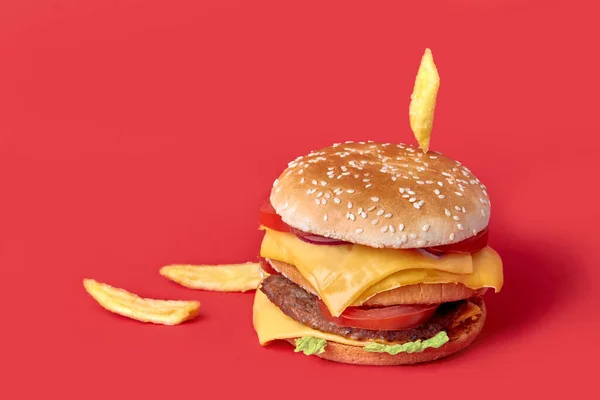 Una gran hamburguesa doble jugosa cae encima de las papas fritas. Fondo rojo. — Foto de Stock