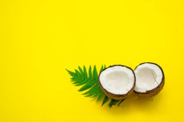 Sarı parlak bir zemin üzerinde hindistan cevizi ve yeşil yapraklar, kozmetik ürünleri için hammaddeler ve yazın sembolü olan sağlıklı yiyecekler.