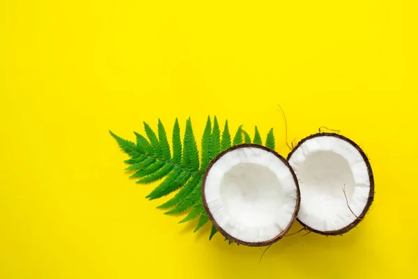 coconut and green leaves on a yellow bright background, raw materials for cosmetic products and healthy food, symbol of summer