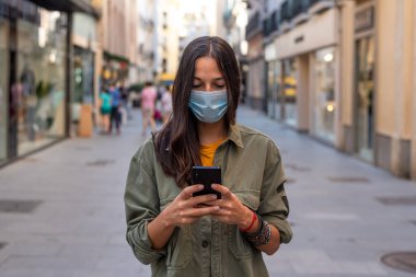 Sokakta cep telefonu kullanırken yüzüne koruyucu maske takan bir kadın.