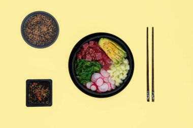 Üzerinde pirinç, avokado, wakame, turp ve salatalık olan ton balığı kabı sarı arka planda.