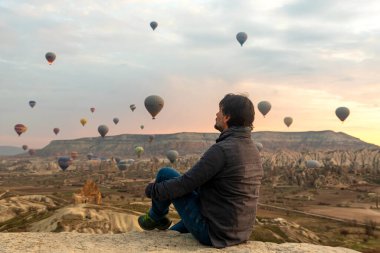 24 Şubat 2018: Kapadokya Vadisi üzerinde uçan harika balonlarla vadi manzarasının tadını çıkaran adam. Goreme, Kapadokya, Türkiye