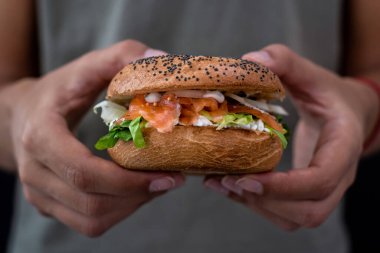 Krem peynirli ve sebzeli somon somunu tutan kadın.