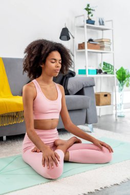 Yoga yapan Afroamerikalı kadın rahat evinde meditasyona poz veriyor.