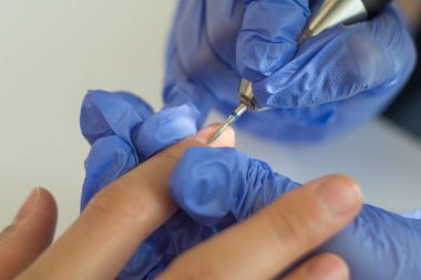 Bir manikürcünün tırnak derisini incelemesi, 27 yaşındaki tırnaklı genç bir kızı tedavi eder. Kadın tırnaklarının güzelliği. Yakından manikürcü, manikürcüleri mekanik bir tırnak tırnağı makinesiyle inceliyor. Plastik eldivenlerde ustalığın yakın plan görüntüsü.