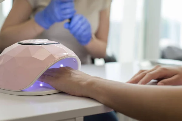 Beautiful nails below UV lamp lamp for nails, covering with ultraviolet of nails close-up. Gel polish coating in a beauty salon. Beauty and health of nails, manicure care