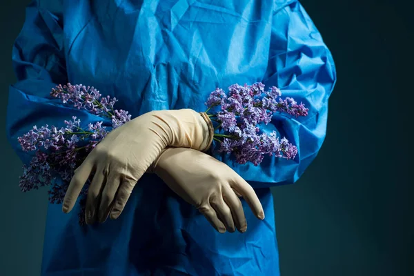 lilac flowers grow from under doctor gloves. Medical concept. The doctor holds yellow flowers in a sterile glove and a blue work suit. Health and healthcare. Operation. Yellow flower. On a blue background. Beauty and health. Aesthetic medicine