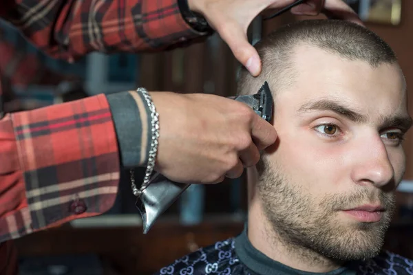 haircut of a young guy with a shield in a barbershop using a typewriter with a nozzle. Barbershop, hair cut by a young guy of twenty seven years old, at the hairdresser, the masters hands trim the hair with a trimmer, trimming his temples Mens haircu