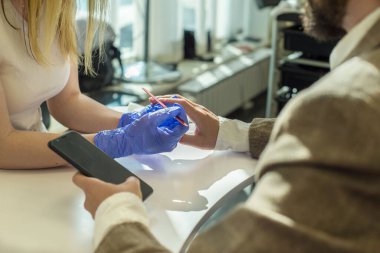 30 yaşında takım elbiseli bir iş adamı akıllı telefon kullanıyor, manikür yapıyor manikür yapan usta bir kız manikürcüde. İş adamı manikürcülüğü kız ustası yapar. Tırnakların güzelliği ve sağlığı.