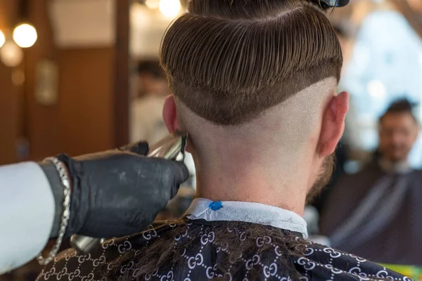 A hairdresser cuts a bearded young guy with a hair trimmer, combing the hair on his head. Work of the master in mens haircut in a barbershop — Stock Photo, Image