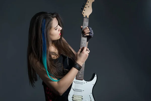 Portrait of a beautiful sexy brunette, in the style of two-handed tapping, plays a riff on an electric guitar. Studio photo on a gray background. Musical girl. Girl composer on an electric guitar. Guitar solo. The sound of a heavy metal guitar.