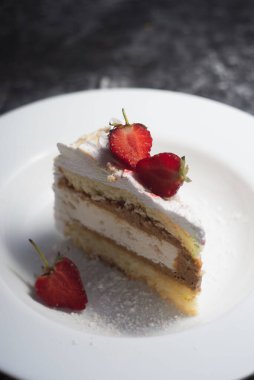 Pasta, pasta, kremalı ve çilekli. Beyaz bir plaka içinde, koyu soyut bir arkaplanda. Yemek fotoğrafı. Dramatik ışık