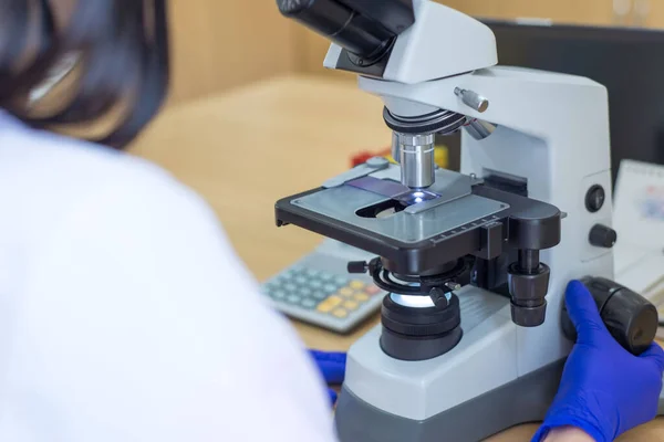 Scientist conducting research taking notes whilst looking through microscope selective focus laboratory assistant is looking through a microscope. Close-up doctor laboratory assistant looking through a microscope, determining a blood test of a patien