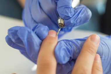 Bir manikürcünün tırnak derisini incelemesi, 27 yaşındaki tırnaklı genç bir kızı tedavi eder. Kadın tırnaklarının güzelliği. Yakından manikürcü, manikürcüleri mekanik bir tırnak tırnağı makinesiyle inceliyor. Plastik eldivenlerde ustalığın yakın plan görüntüsü.