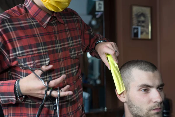保護マスクのコロナウイルス美容師が床屋で若い男を切りました コロナウイルスのパンデミックの間のヘアケア Covid 美容師 理容師 27歳の男性のための散髪 短い毛 劇的な光の中で — ストック写真