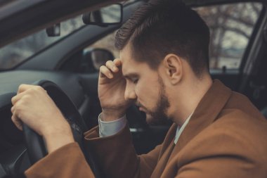 30 yaşında genç bir adam, başını tutuyor, başı ağrıyor, araba kullanıyor. Araba kullanırken sağlıksız. Sıcak renklerde, modaya uygun, alışılmadık bir ton. Araba kullanan bir iş adamı. İş için ofise giderken, işadamı hastalandı. Davulun tehlikesi