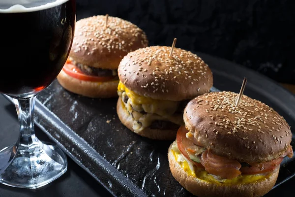 mug of beer with hamburger and fries close-up, beer glasses with craft dark and light beer with foam, against a background of burgers, with a variety of ingredients, including shyomga, beef meat patty, cheese burger. In a rustic style, against a blac