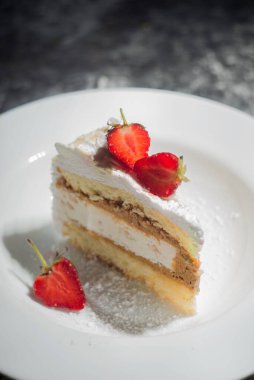 Pasta, pasta, kremalı ve çilekli. Beyaz bir plaka içinde, koyu soyut bir arkaplanda. Yemek fotoğrafı. Dramatik ışık