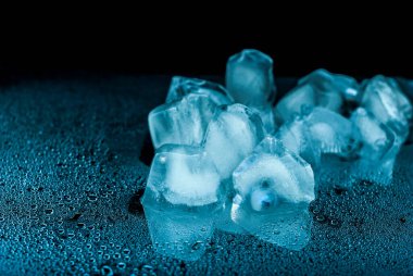 Buz küpleri siyah masa arkaplanına yansıyor. Bardağa bir damla su. Yakın çekim.