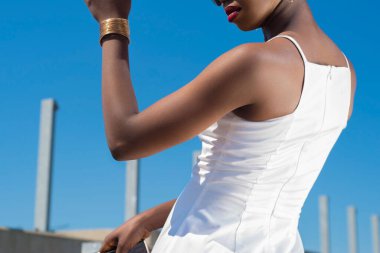 Beyaz elbiseli moda Afrikalı siyahi kız, mavi gökyüzünün arka planında poz veriyor. Beyaz elbiseli, mavi gökyüzüne karşı poz veren Afro-Amerikalı genç bir kız model. Kısa elbiseli seksi Afrikalı Amerikalı kadın.