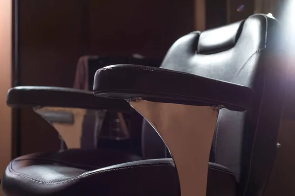 a hairdressing chair made of brown leather, under a ray of light, in a barbershop, a hairdressing salon. Close-up, barbershop interior. Hair cutting, shaving, hair care interior of luxury beauty salon - workplace hairdresser