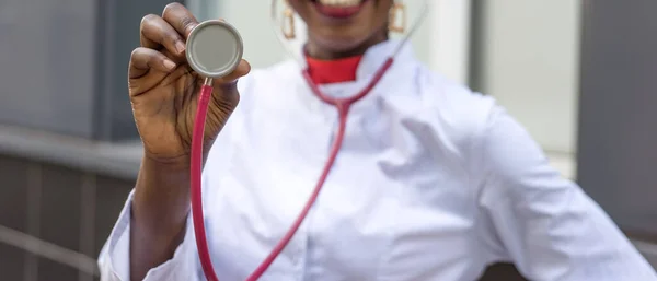 Detailní záběr ruky afroamerického lékaře s auskulační fonendoskopickou membránou. Lékařský koncept. Černá lékařka žena v bílém kabátě s fonendoskopem — Stock fotografie