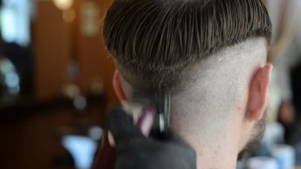 Een kapper knipt een bebaarde jongeman met een haarknipper, kamt het haar op zijn hoofd. Werk van de meester in mannen kapsel in een kapperszaak — Stockvideo