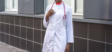 Beyaz önlüklü, elinde fonendoskop olan genç bir kadın doktor, hastane arka planında, bir mezarda tıbbi belgeler için bir klasör tutuyor..