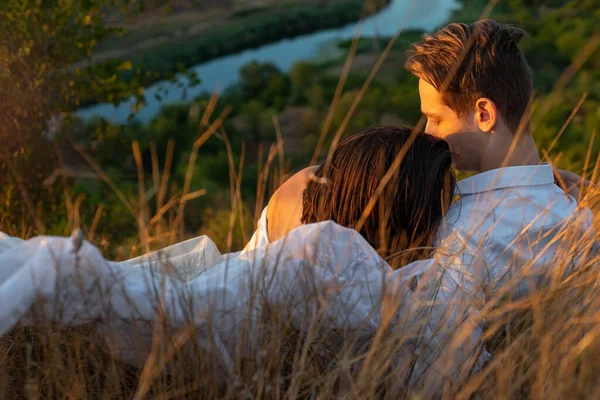 half portrait of a beautiful couple of guy and girl lying in the grass. Against the backdrop of the setting sun on a summer evening. White dress of the bride. Young couple of twenty two years old, in a field of grass. girl with a guy on green grass,