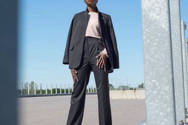 Genç siyahi bir kız, iş tarzında, mavi gökyüzüne karşı sokakta poz veriyor. Moda ve ofis, iş tarzı, ofis kıyafetleri, moda tasarımı, siyah genç kız modeli, açık hava kızı