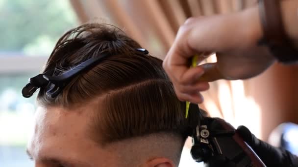Un peluquero corta a un joven barbudo con un cortador de pelo, peinándose el pelo en la cabeza. El trabajo del maestro en mens corte de pelo en una peluquería — Vídeos de Stock