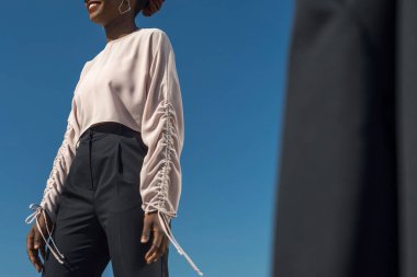 Genç siyahi bir kız, iş tarzında, mavi gökyüzüne karşı sokakta poz veriyor. Moda ve ofis, iş stili, ofis kıyafetleri, moda tasarımı, siyahi genç kız modeli