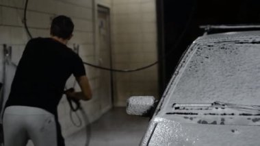 Adam arabanın üzerindeki sabunu bir kersher 'ın baskısı altında bir jet suyla yıkıyor.