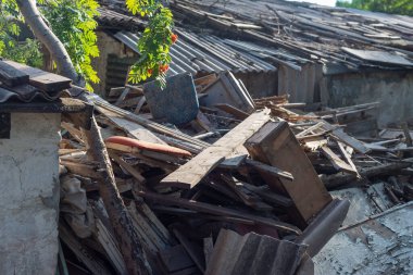Eski tahtalarla dolu çöp yığını, binanın eski duvarlarının arka planına karşı. Eski tahtalarla çevre kirliliği. Organik ahşap atık yığını enkaz yığını, tahta parçaları, kontrplak ve beton bloklar. Kereste, çöp, yangın