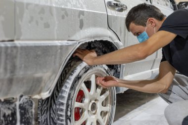 Coronavirus arabayı temizliyor, arabayı sabun solüsyonundan kersher ile yıkıyor. Otomotiv teknisyenlerinin karantina döneminde yaptığı iş. Kapıdaki araba yıkama için yüksek basınçlı su püskürtücüsü tutan adamın 19 yakın çekimi. Temassız benlikler.