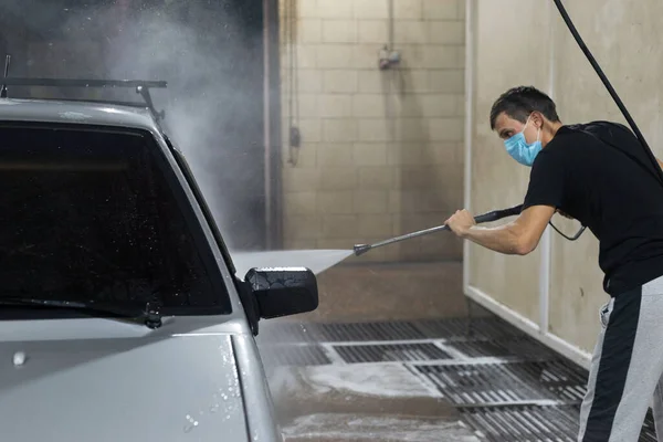 coronavirus cleaning of the car, washing the car body with a kersher from soap solution. The work of auto technicians during the quarantine period covid 19 Close-up of man holding a high-pressure water sprayer for door car washing. Contactless self-s