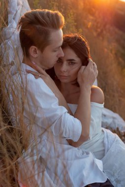 22 yaşında genç, güzel bir erkek ve bir kızın portresi. Beyaz elbiseler giyiyordu. Çimenli bir tarlada, bulutlu bir gökyüzünün ve batan güneş ışınlarının arka planında. Amorous çifti. Romantik bir çift genç adam ve kız.