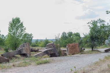 Metal elementlerle taştan yapılmış antik beton sütunlar. Ormanın arka planına karşı. Betonla çevre kirliliği. Beton bir köprü ormana giden yolu tıkıyor. Çevreye çöp atılmasını yasaklamak