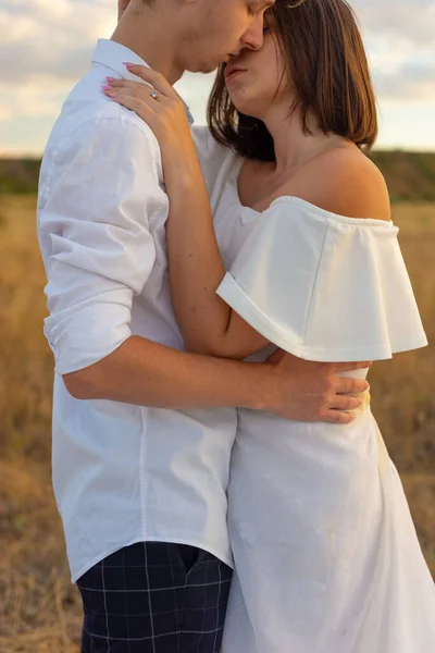 kiss of a girl and a guy. close-up portrait. Young couple of guy and girl in white clothes, in the field. Against the backdrop of a cloudy sky. Kissing couple of young people, twenty-two years old. Young Couple in love