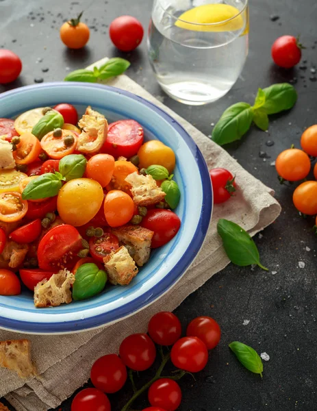 Panzanella paradicsom saláta koktélparadicsommal piros, sárga, narancs, kapribogyóval, bazsalikommal és ciabatta kenyérkockákkal. nyári egészséges ételek. — Stock Fotó