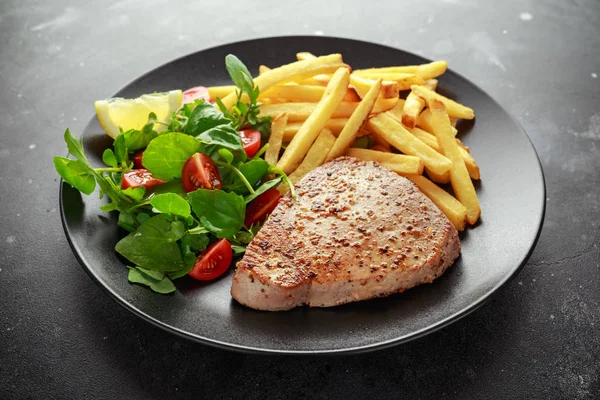 Bifes de atum frito na placa preta com verde fresco, salada de tomate, limão e batatas fritas. alimento saudável para o mar — Fotografia de Stock