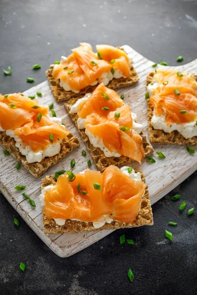 Homemade Crispbread toast with Smoked Salmon and soft chees, chives on white board.